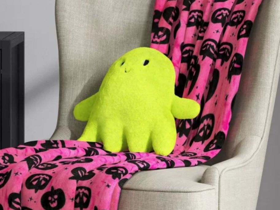 A green Ghost Target Halloween Throw pillow on a chair with a neon pink halloween blanket