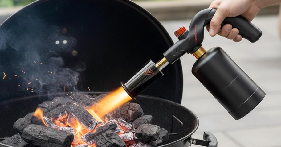 Person using a propane torch on a grill.