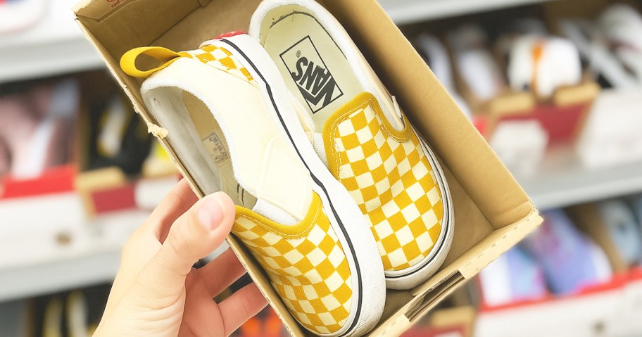 hand holding up a shoe box with white and yellow checkerboard print kids shoes inside