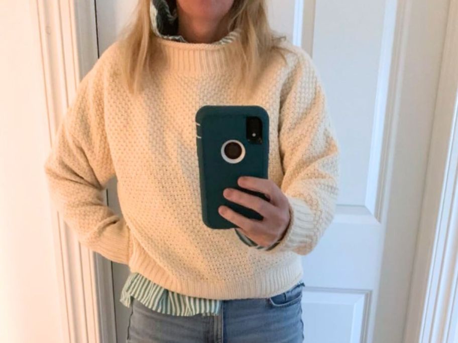 A woman wearing a white sweater taking a selfie