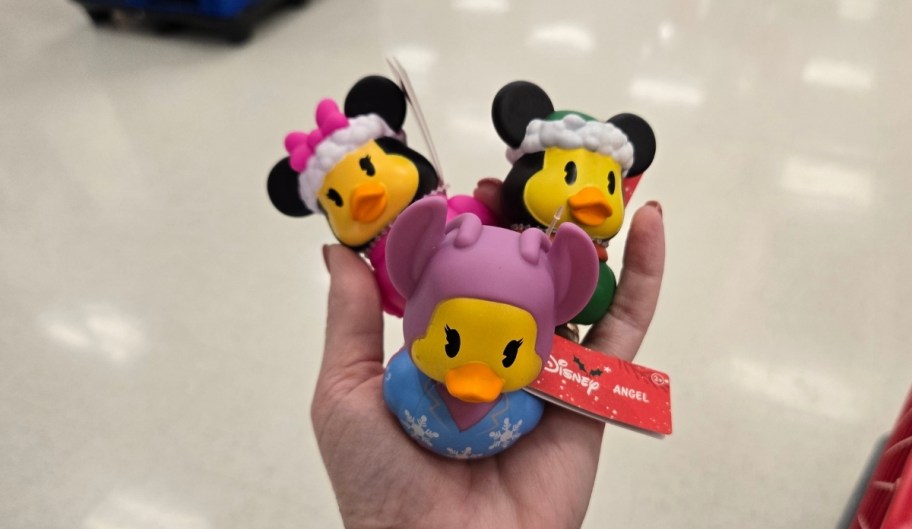 a womans hand holding 3 disney holiday themed rubber duckies