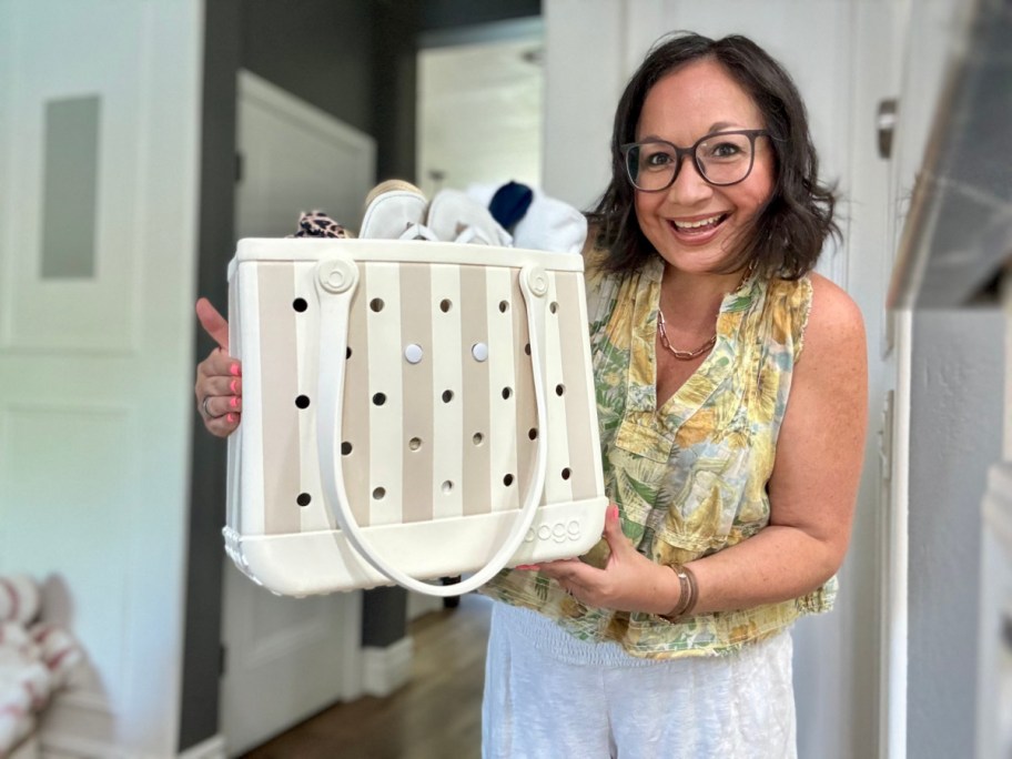 smiling woman holdng up a white and tan striped bogg bag