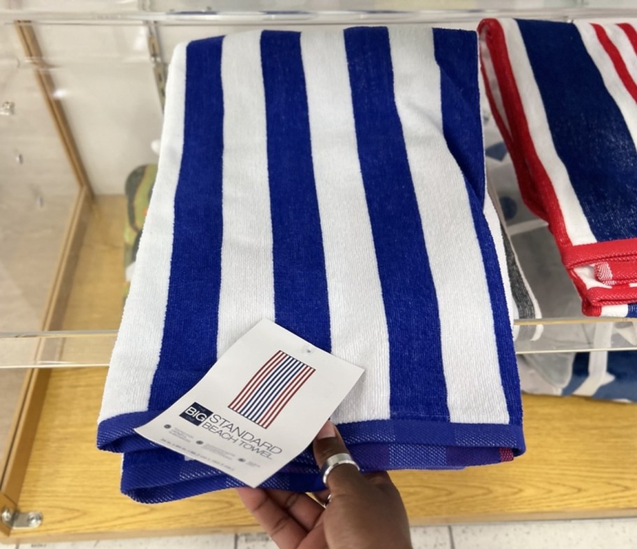 a womans hand grabbing a striped beach twel from astore shelf
