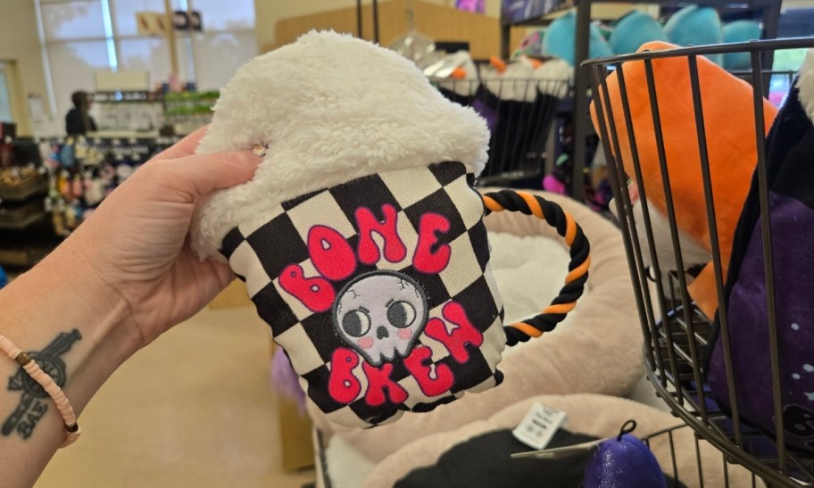 a woman's hand holding a bone brew plush dog toy