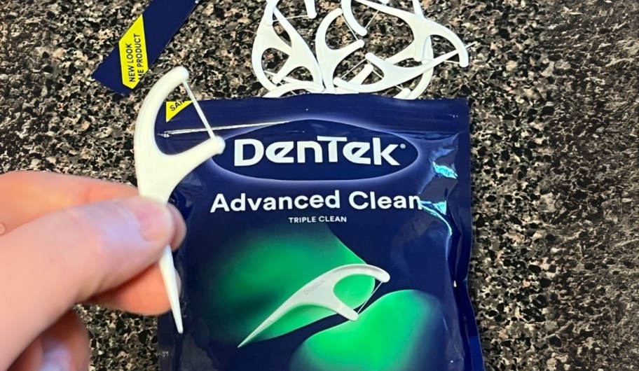 a hand holding a white dentek dental floss pick