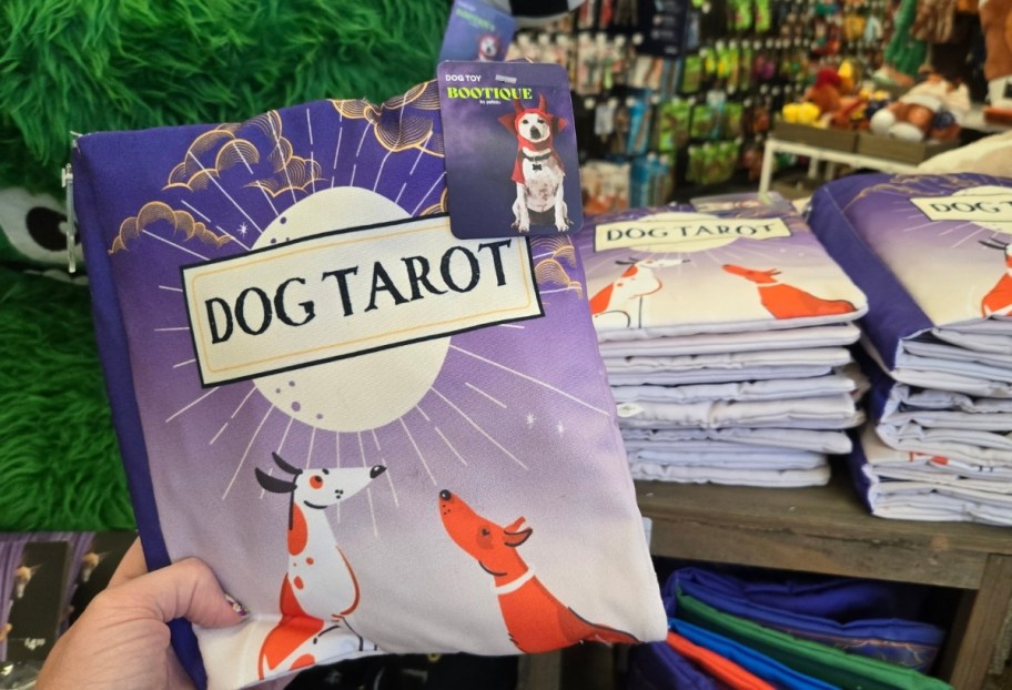 a womans hand holding a tarot book plush dog toy