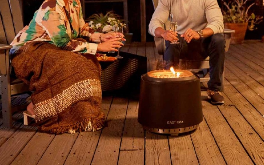 two people sitting next to a firepit in the evening drinking wine