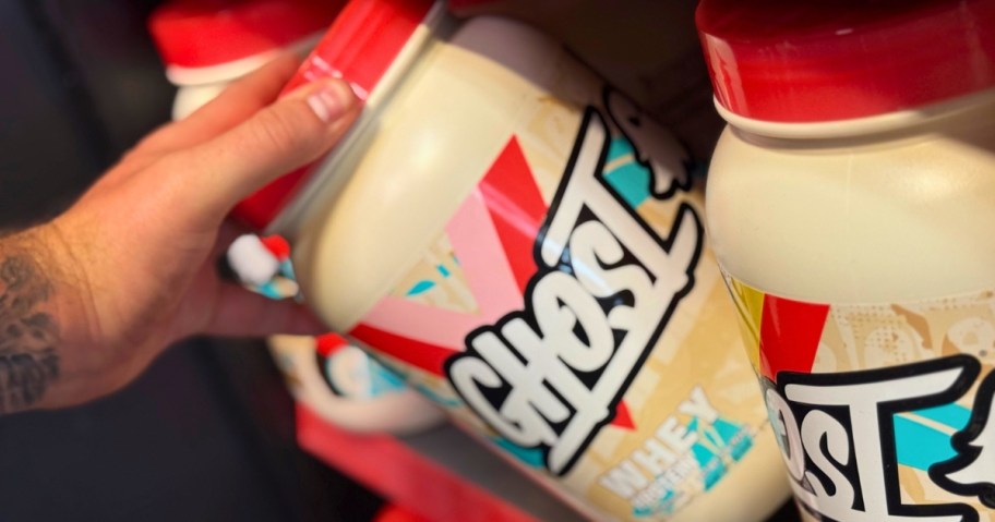 hand pulling a container of GHOST protein powder off a store shelf