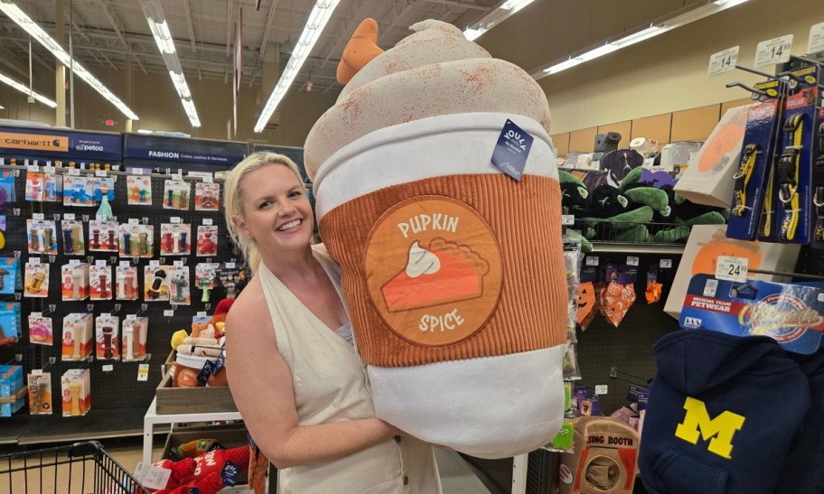 a woman holding a giant pumpkin spice latte dog toy