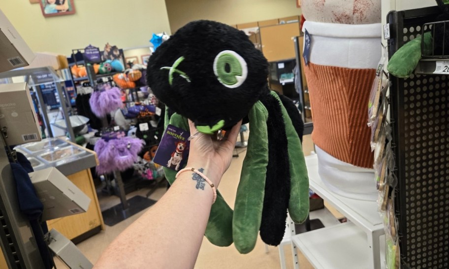 a woman's hand holding a green and black plush spider dog toy