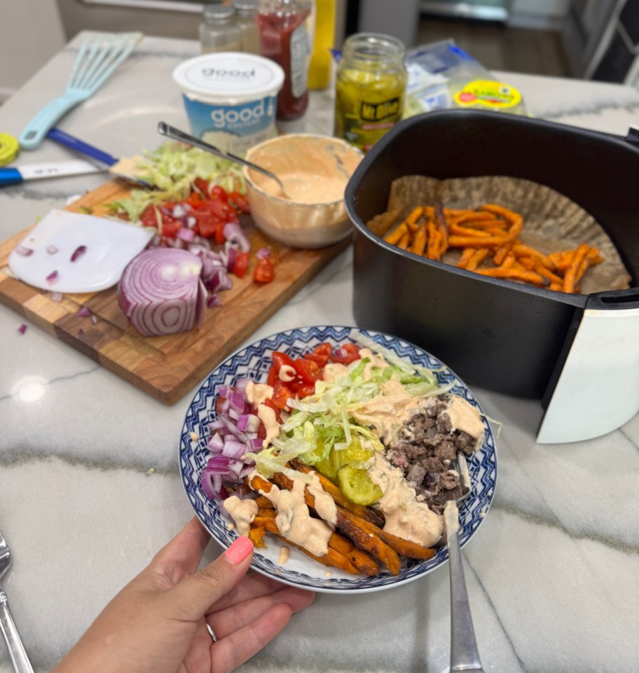 holding a loaded burger bowl next to air fryer fries