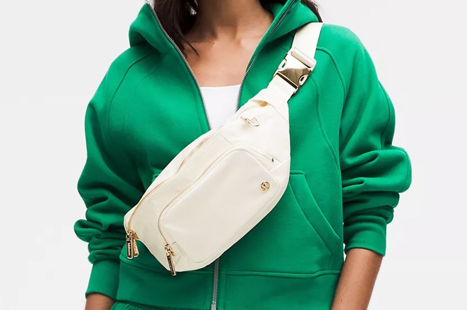 woman in a green zip-up sweatshirt with a white belt bag across her chest