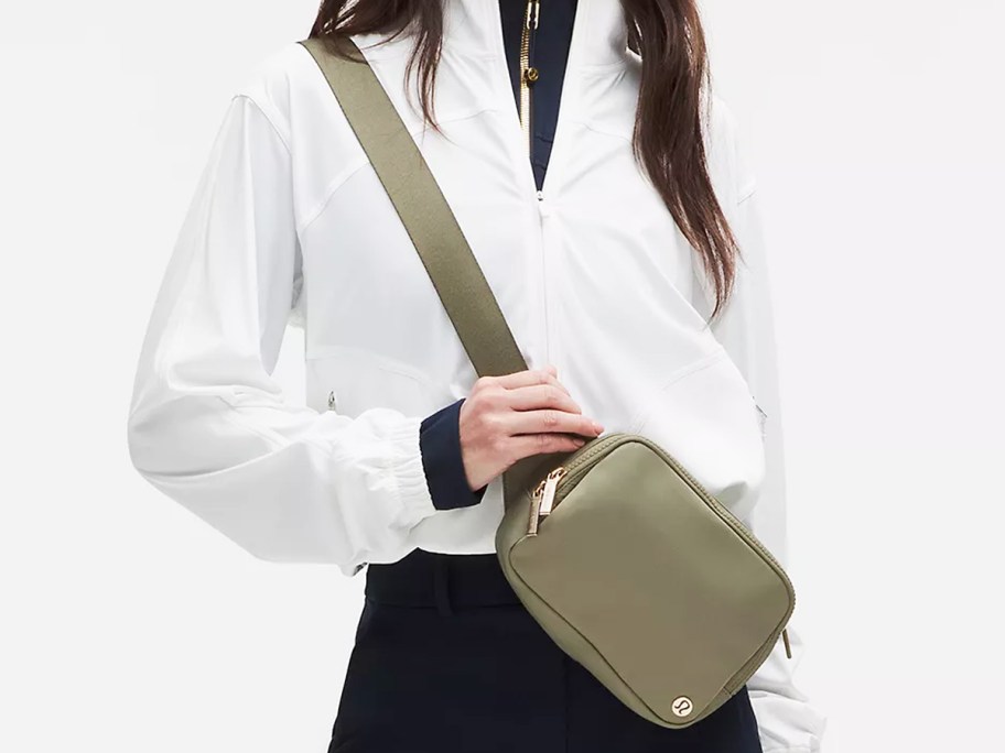 woman in a white jacket with an olive green belt bag across her chest