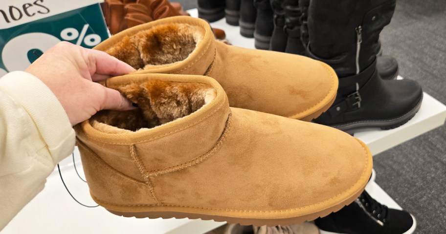 hand holding up a pair of tan boots in store