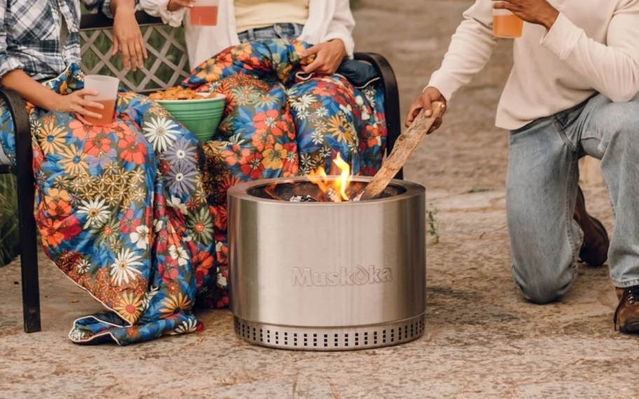 3 people sitting on a patio next to a smokeless fire p0it