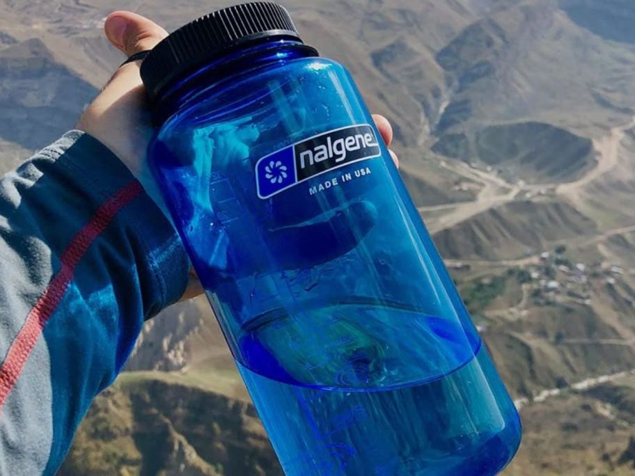 nalgene water bottle in persons hand in front of the mountains
