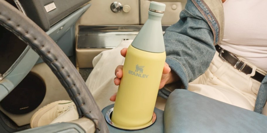 hand reaching for yellow and green stanley water bottle in car