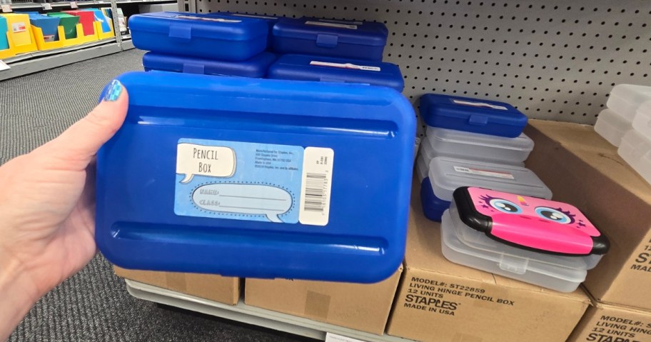 hand holding a blue pencil box, more colors on a shelf behind it in a store