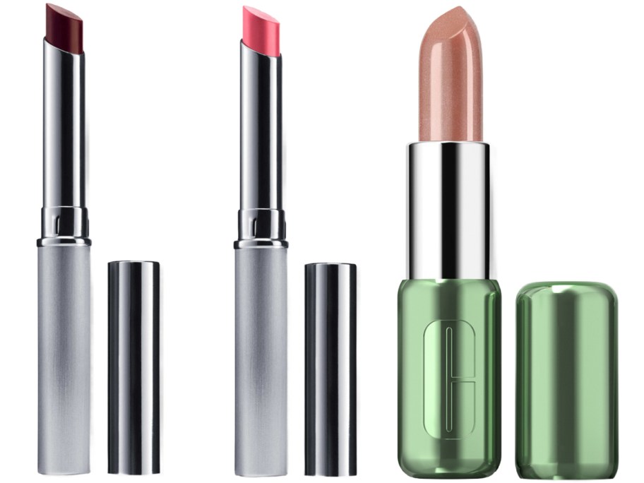 Three open lipsticks standing upright next to their caps: two in thin silver tubes with dark red and pink shades, and one in a green Clinique tube with a shimmery nude shade.