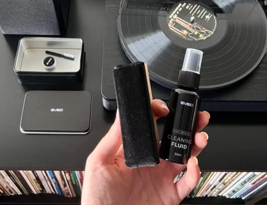 Hand holding vinyl record cleaning brush and spray over turntable