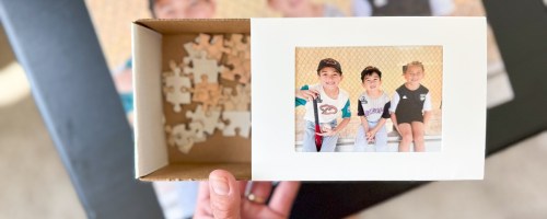 hand holding a keepsake box with a photo of kids on it, puzzle pieces inside the box and a partially put together photo puzzle behind it