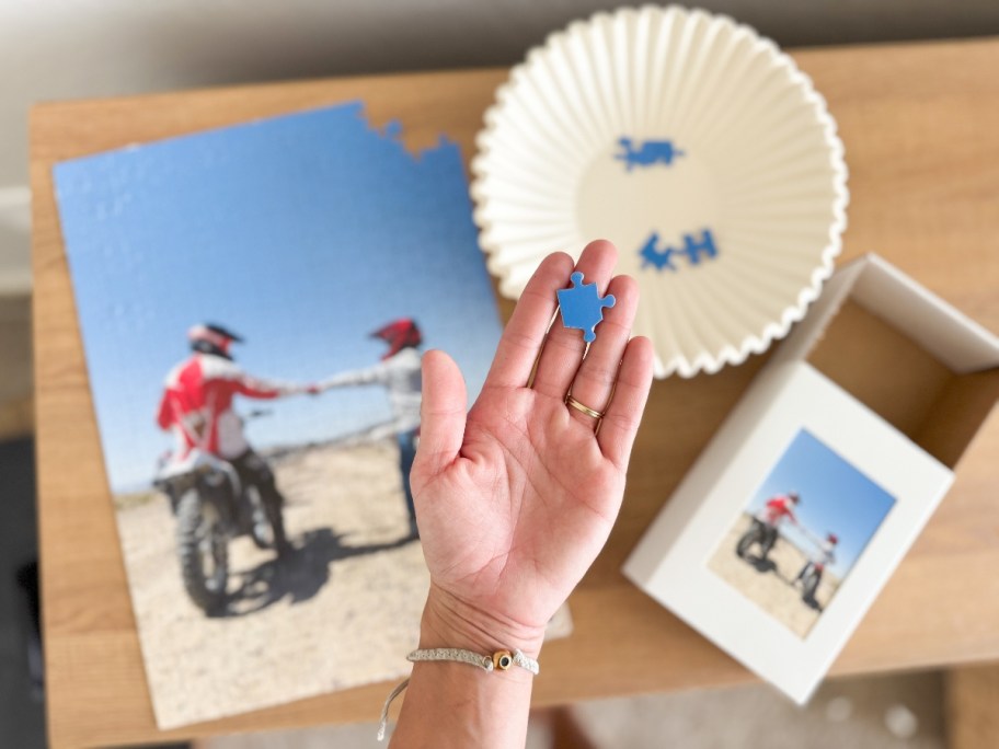 hand holding puzzle pieces of a photo puzzle and a keepsake box with the photo on it on a table behind