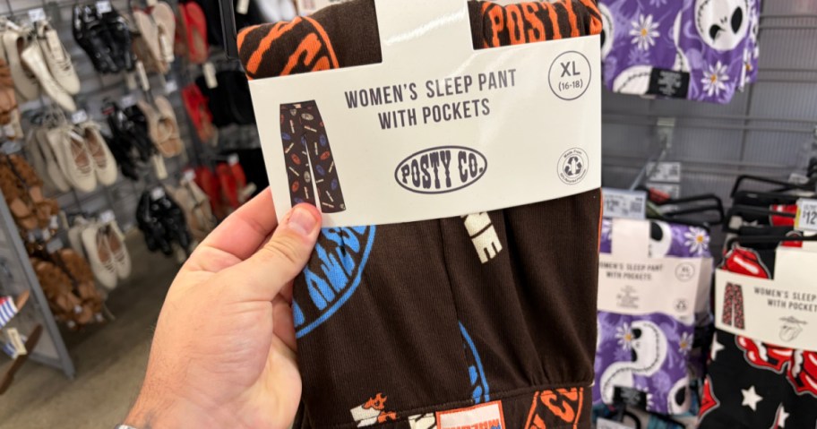 A person holding a package of women's sleep pants with pockets, labeled "Posy Co," in an XL size. The background shows various clothing items displayed in a store.