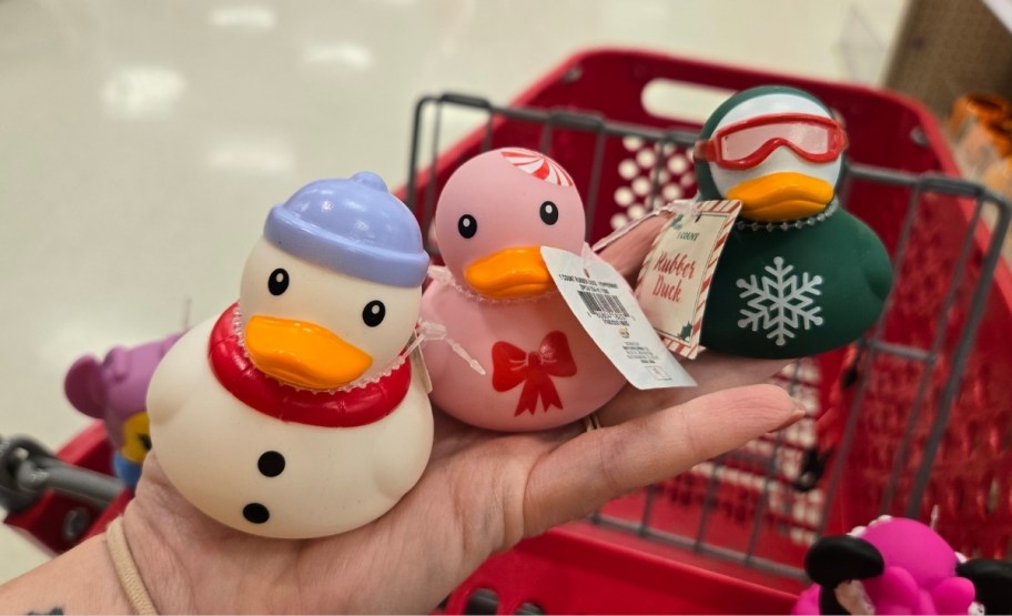 a womans hand holding 3 different holiday themed rubber duck