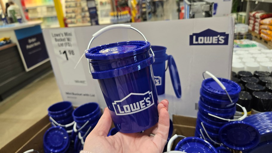 holding a blue mini-bucket in front of Lowe's signage