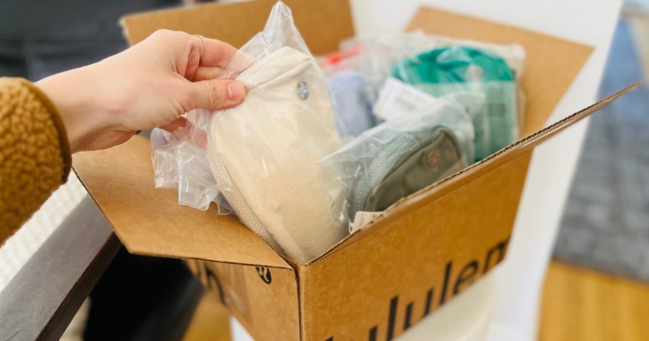 hand pulling a lululemon bag out of a box filled with several items