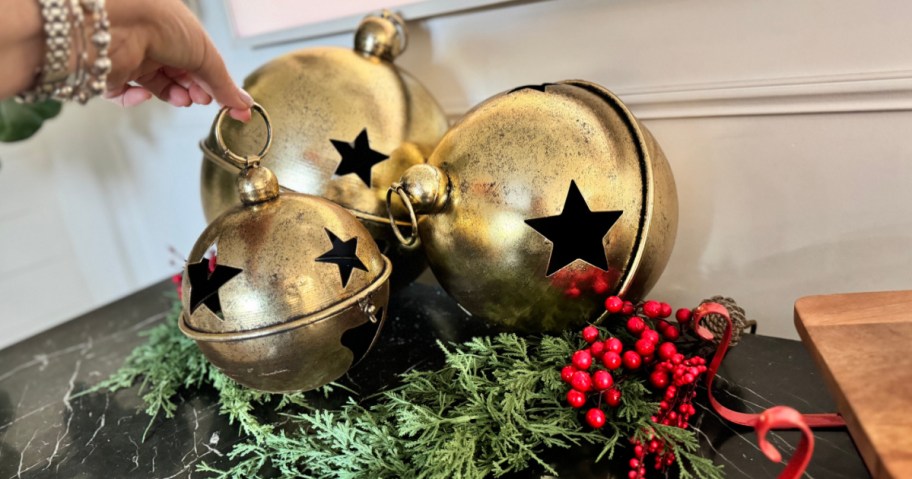 Three gold antique jingle bells on tabletop next to red Holly