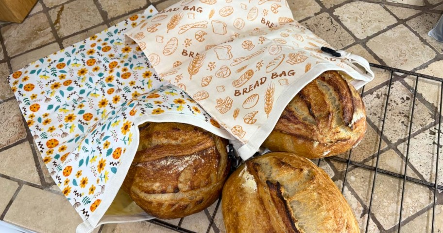 loaves of fresh baked bread sitting in reusable beeswax bread bags on kitchen counter