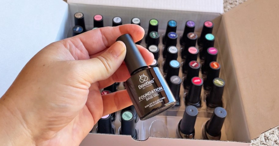 holding a bottle of gel base coat with lots of colors in box in background