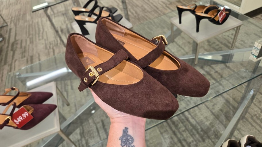 hand holding up pair of brown suede shoes