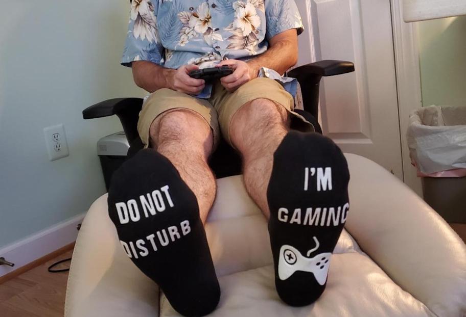 Person with feet on ottoman wearing do not disturb I'm gaming socks 