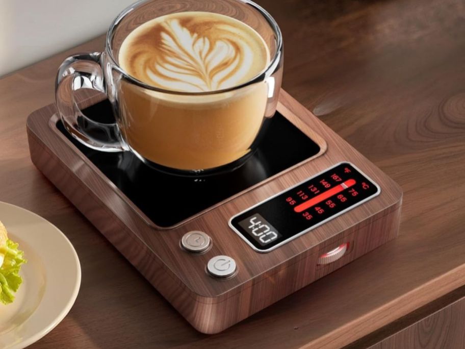 A latte in a clear mug on top of a rectangle coffee warmer