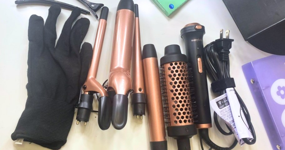 a curling iron set with different wand attachments and a brush attachment, a heat-resistant glove and hair clips on a counter