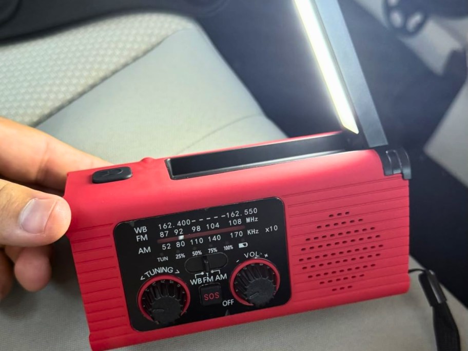 a hand holding an Emergency Weather Radio that has a flashlight on it