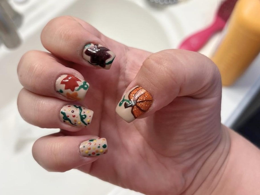 hand showing off fingernails painted with fall themed nail colors and designs