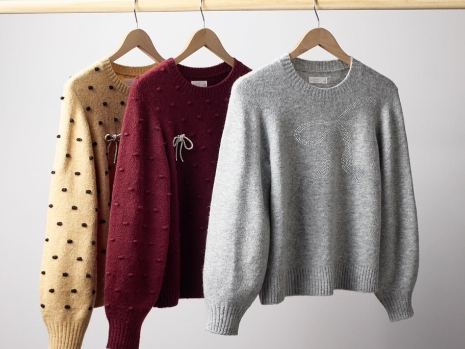 three sweaters hanging on hangers