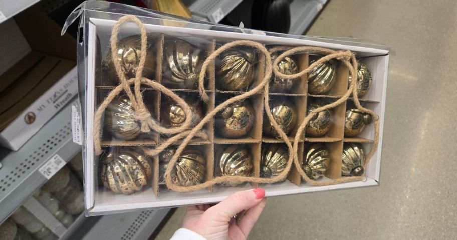 a person holding a box of golden ball ornaments