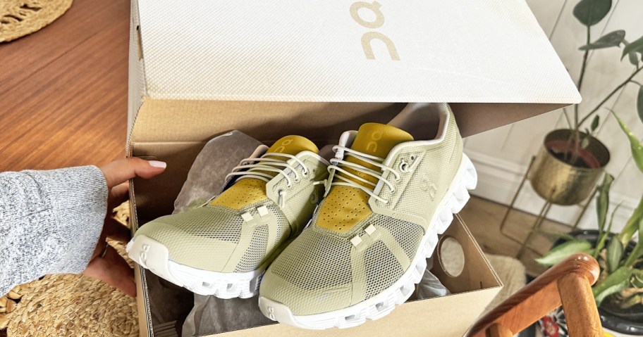 hand holding an opened shoe box with yellow running shoes inside