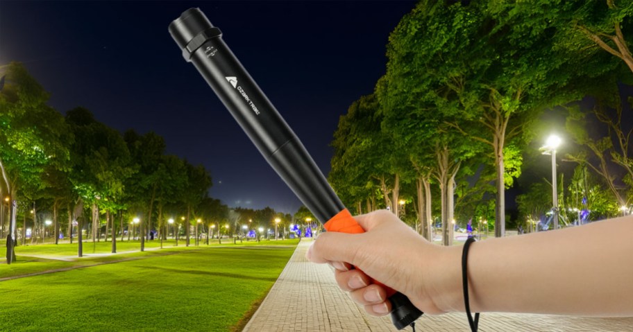 Ozark Trail Focusing LED 200 Lumens 12-inch Bat Flashlight being held by a woman in a park at night