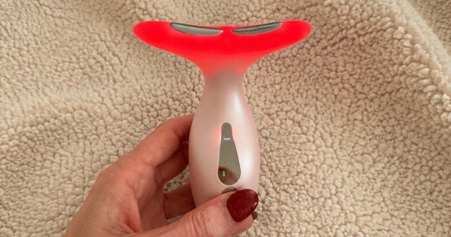 hand holding up a red light therapy wand with a blanket in the background