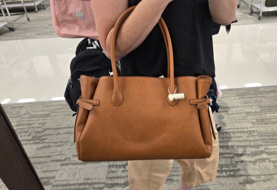 arm holding up brown satchel bag in store