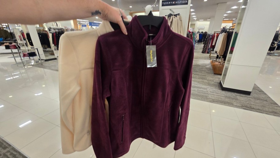 hand holding cream and burgundy fleece jackets on hanger in store