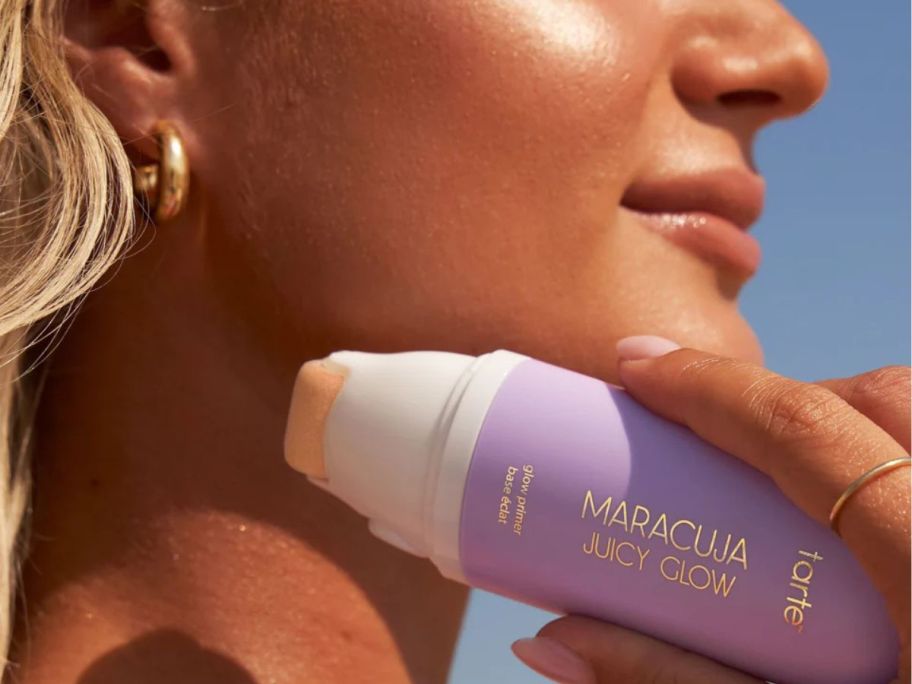 woman holding a tarte Maracuja Juicy Glow Primer next to her face