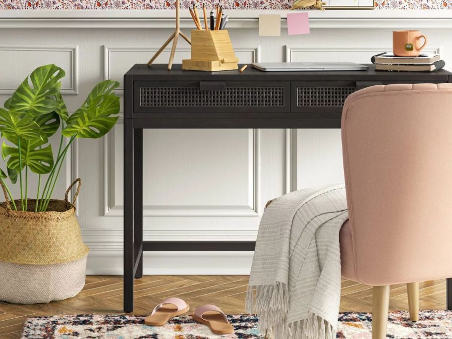 A dark-colored desk in a light room with a pink chair 
