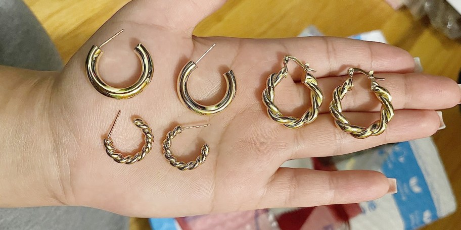 hand holding pairs of gold hoop earrings 