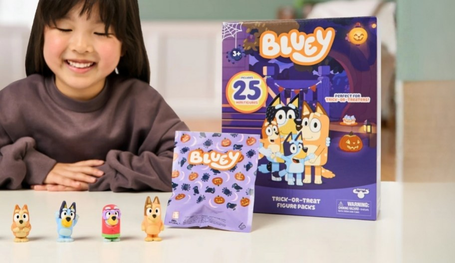 little girl playing with mini Bluey figures next to the box they come in